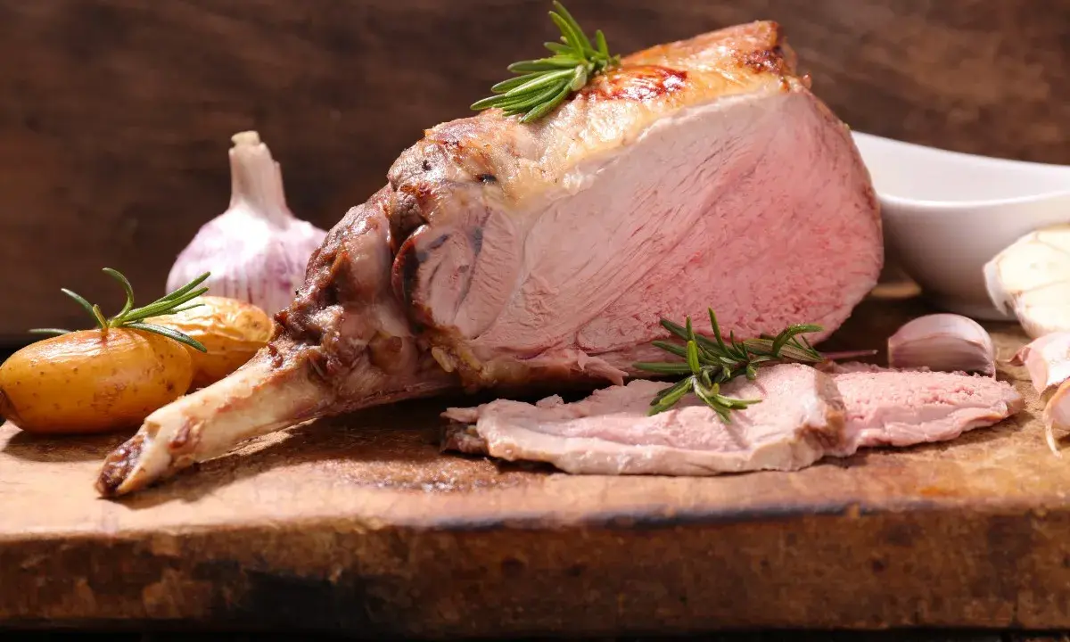 Un gigot d'agneau rôti, tendre et juteux, avec des pommes de terre et de l'ail. Ce gigot qui pleure de délice est prêt à être dégusté.
