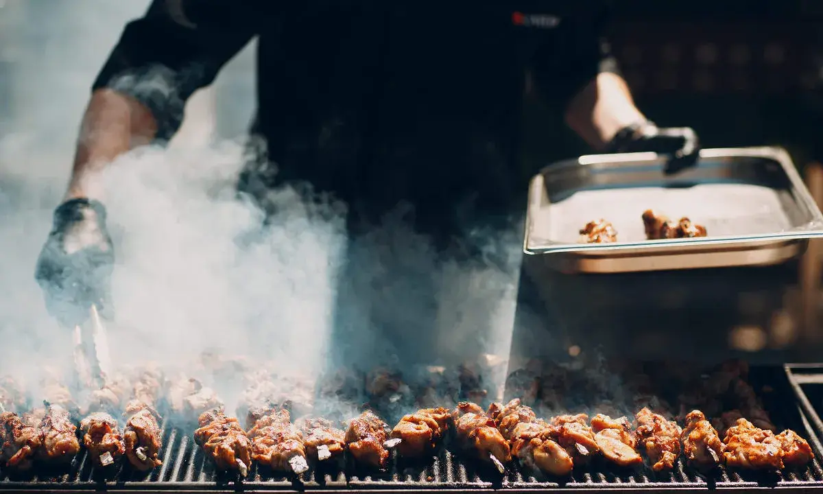 Un chef prépare un délicieux barbecue italien, des brochettes de viande fumantes sur le grill.