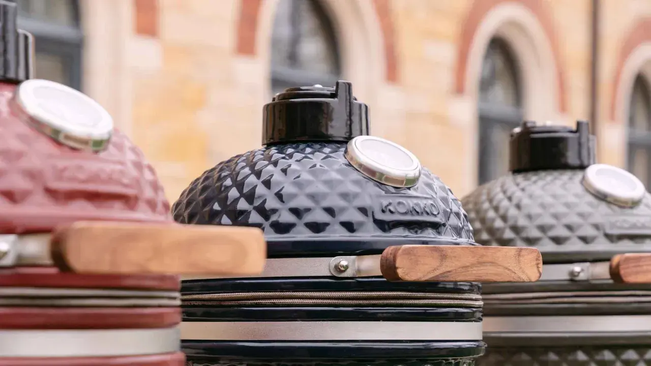 Trois barbecues kamado de couleurs différentes, prêts pour un avis. Le noir est au centre, le rouge à gauche, le gris à droite.