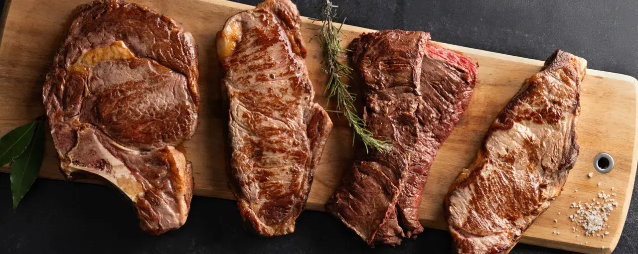 Quatre pièces de viande de saison octobre, grillées à la perfection, sur une planche en bois avec des herbes et du sel.