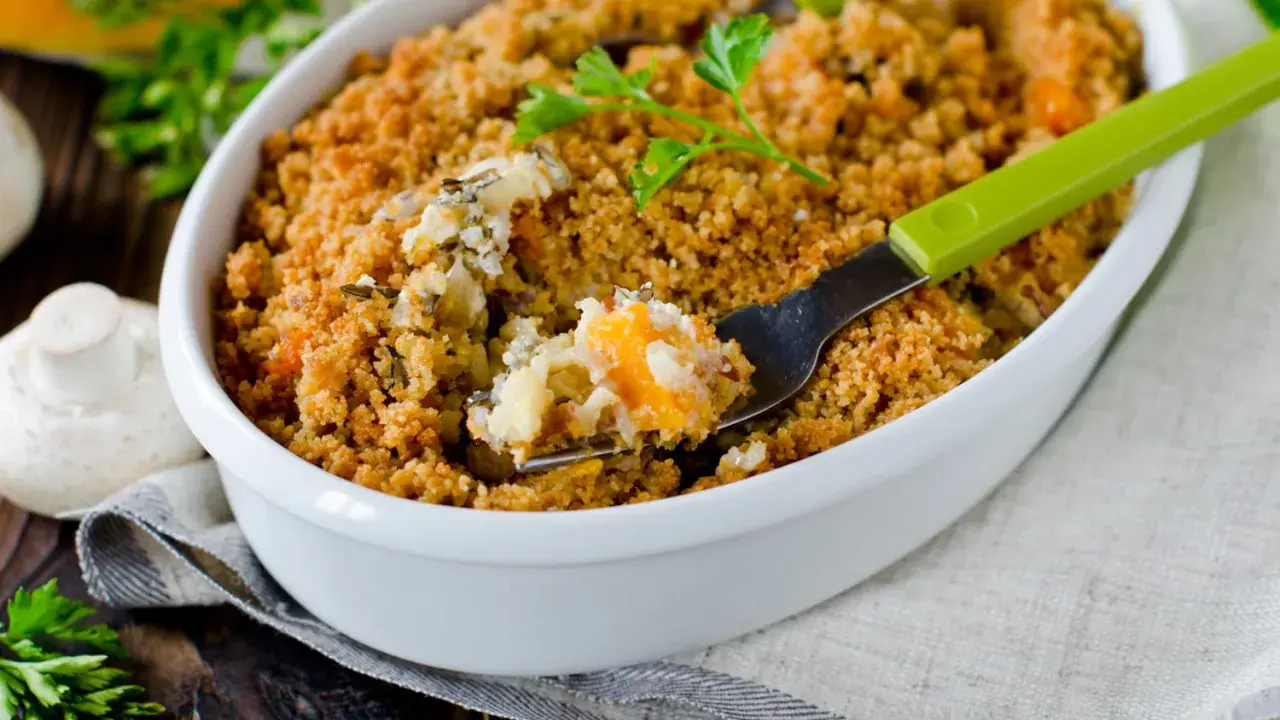 Un délicieux crumble salé aux légumes et riz, servi dans un plat blanc, avec une fourchette verte prête à déguster.