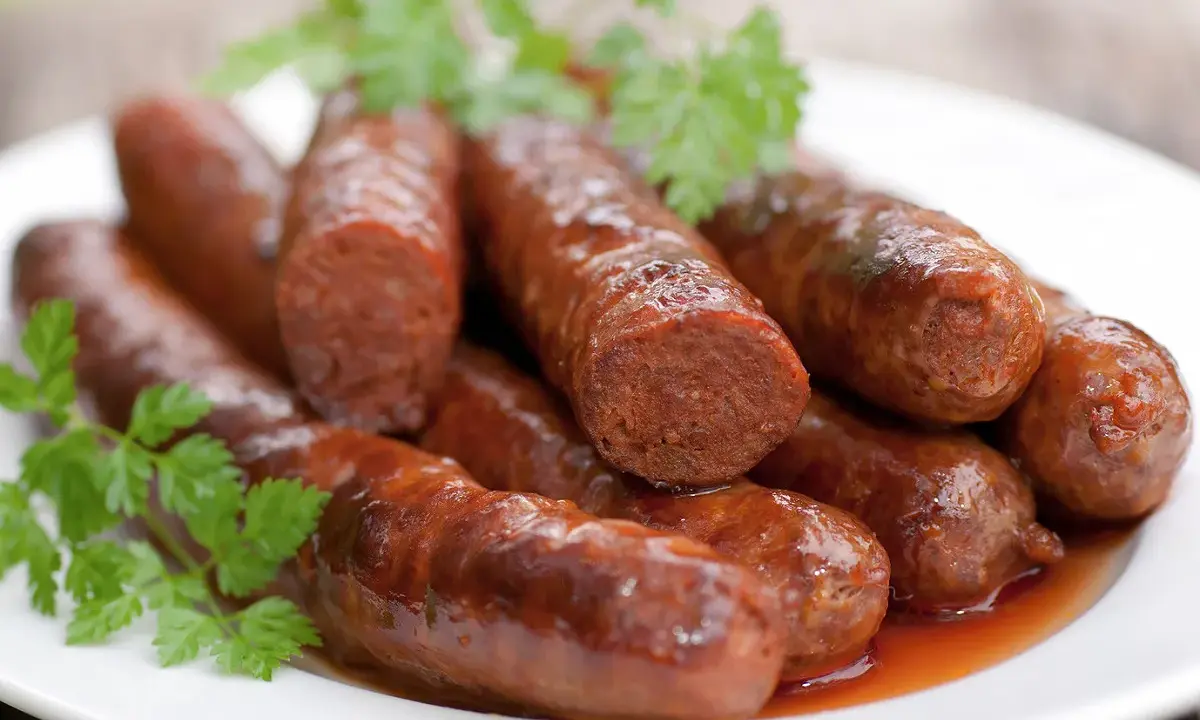 Assiette de merguez au four, dorées et juteuses, garnies de persil frais. Un délice prêt à être dégusté.