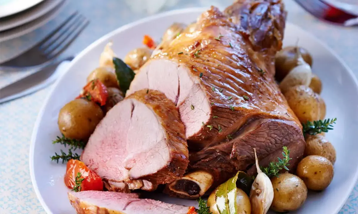 Un gigot d'agneau rôti, tranché, servi avec des pommes de terre nouvelles, tomates et ail. Parfait pour savoir que faire avec des morceaux de gigot d'agneau.