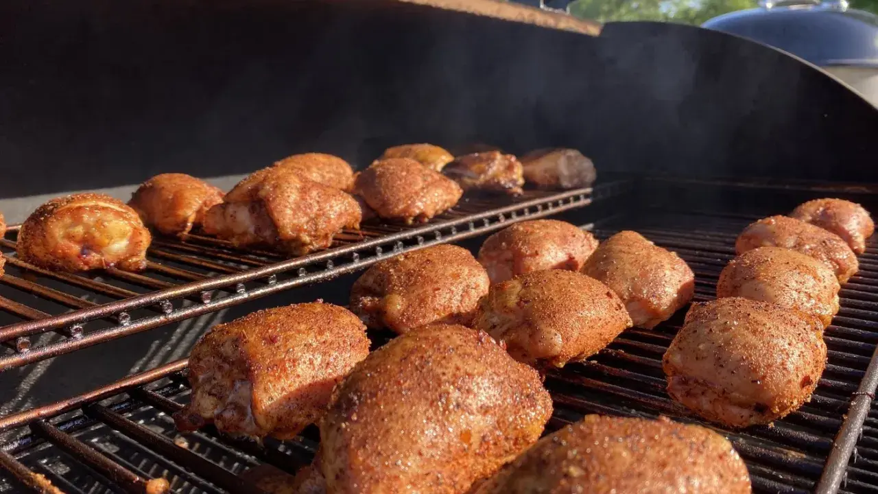 De nombreuses cuisses de poulet désossées, assaisonnées et grillées, fument sur un barbecue par une journée ensoleillée.