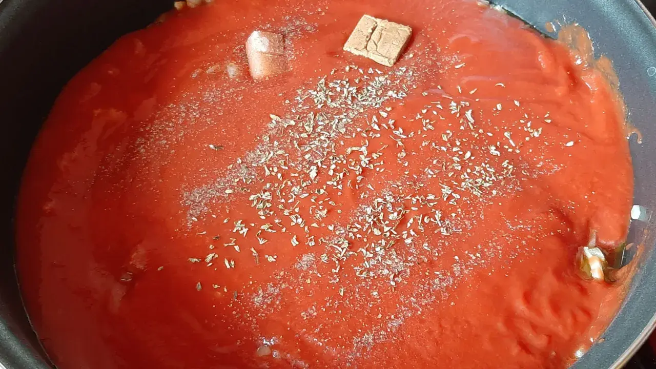Sauce tomate maison mijote dans une poêle, agrémentée d'herbes et d'un cube de bouillon.