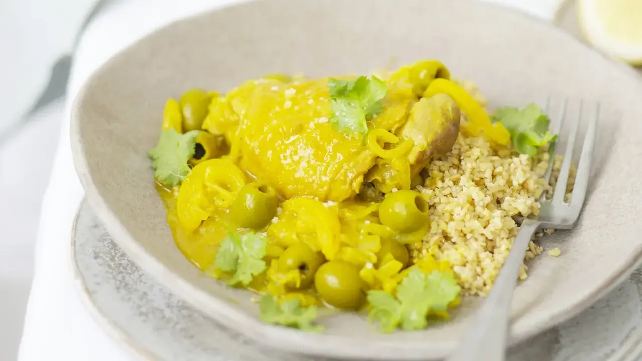 Un plat de tajine poulet citron, garni d'olives vertes et de coriandre fraîche, servi avec du couscous.