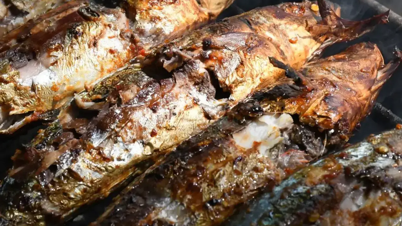 Plusieurs poissons entiers, dorés et appétissants, cuisent sur un barbecue au charbon. Quel poisson au barbecue charbon, une merveille !