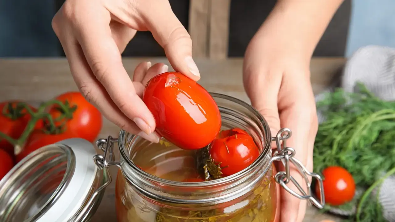 Mains ajoutant une tomate dans un bocal pour une recette de tomate farcie le parfait.