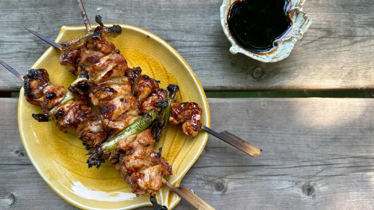 Brochettes yakitori savoureuses, laquées et grillées, servies sur une assiette jaune avec une sauce foncée à côté.