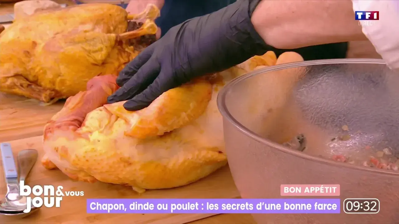 Main d'un cuisinier en gant noir préparant une farce poulet avec abats. Un chapon doré est à côté.