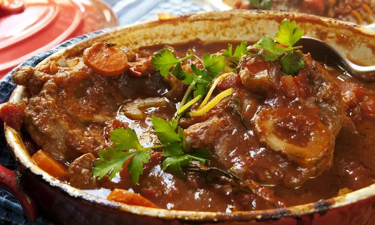 Un plat mijoté de veau marengo traditionnel, avec des morceaux de viande tendres dans une sauce tomate riche, garni de persil frais et de carottes.