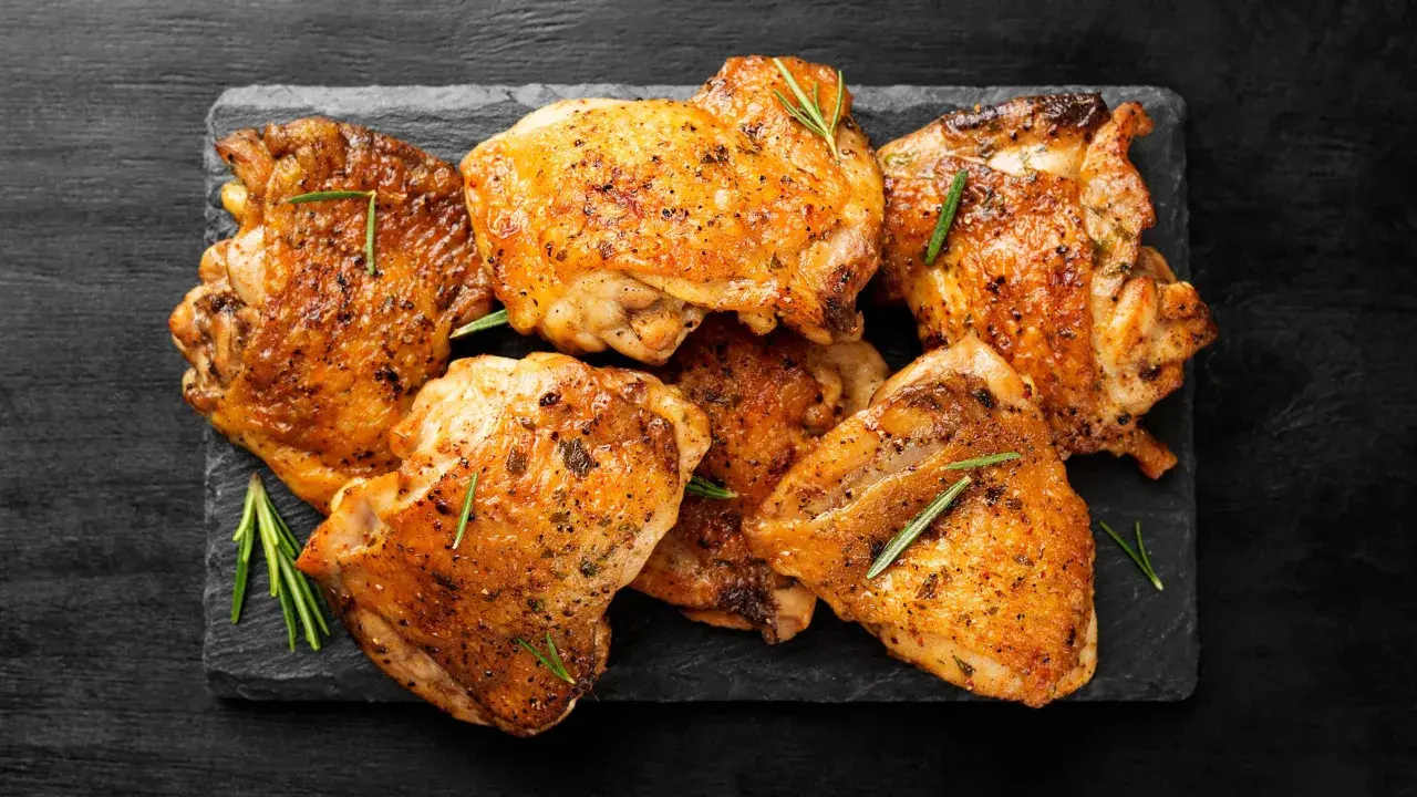 Pile de haut de cuisse de poulet grillé, assaisonné d'herbes et de poivre, sur une ardoise noire.