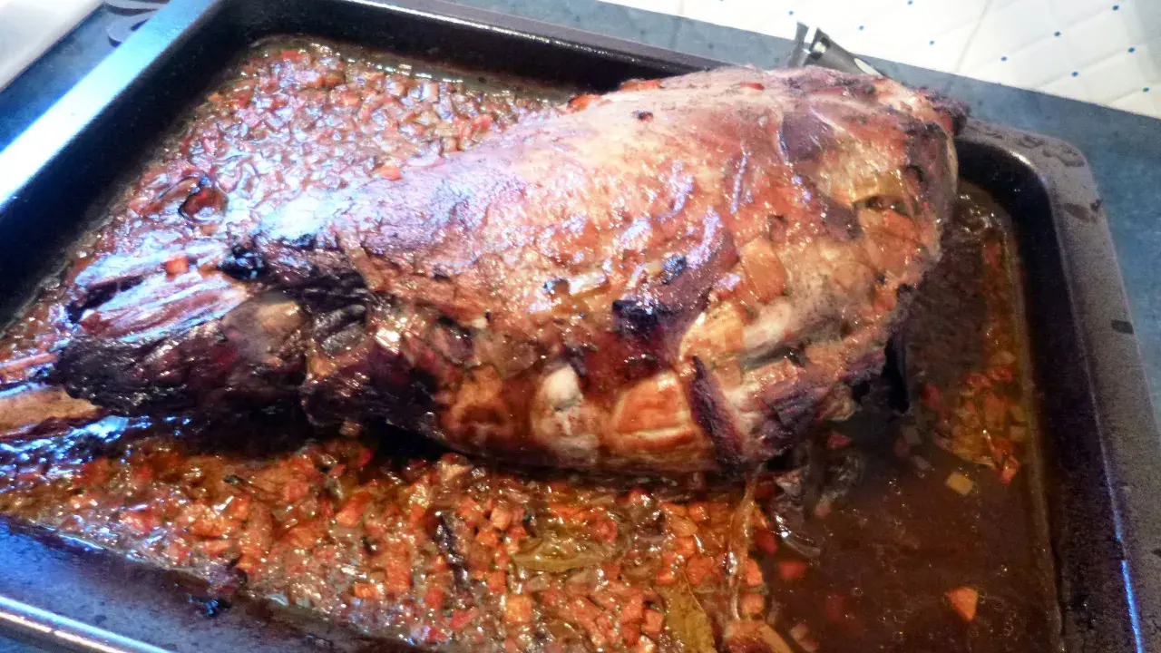 Gigot de sanglier rôti 7h, baignant dans son jus avec des légumes coupés. Un plat savoureux prêt à être dégusté.