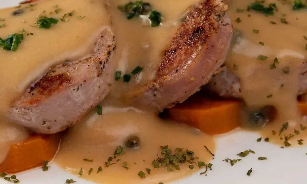 Tranches de gigot d'agneau nappées d'une sauce onctueuse au fond de veau, parsemées de persil et de câpres, sur un lit de carottes.