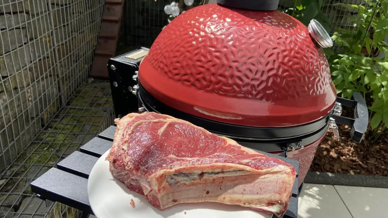 Une belle côte de bœuf crue attend sur une assiette blanche, prête à être grillée sur le barbecue rouge vif.