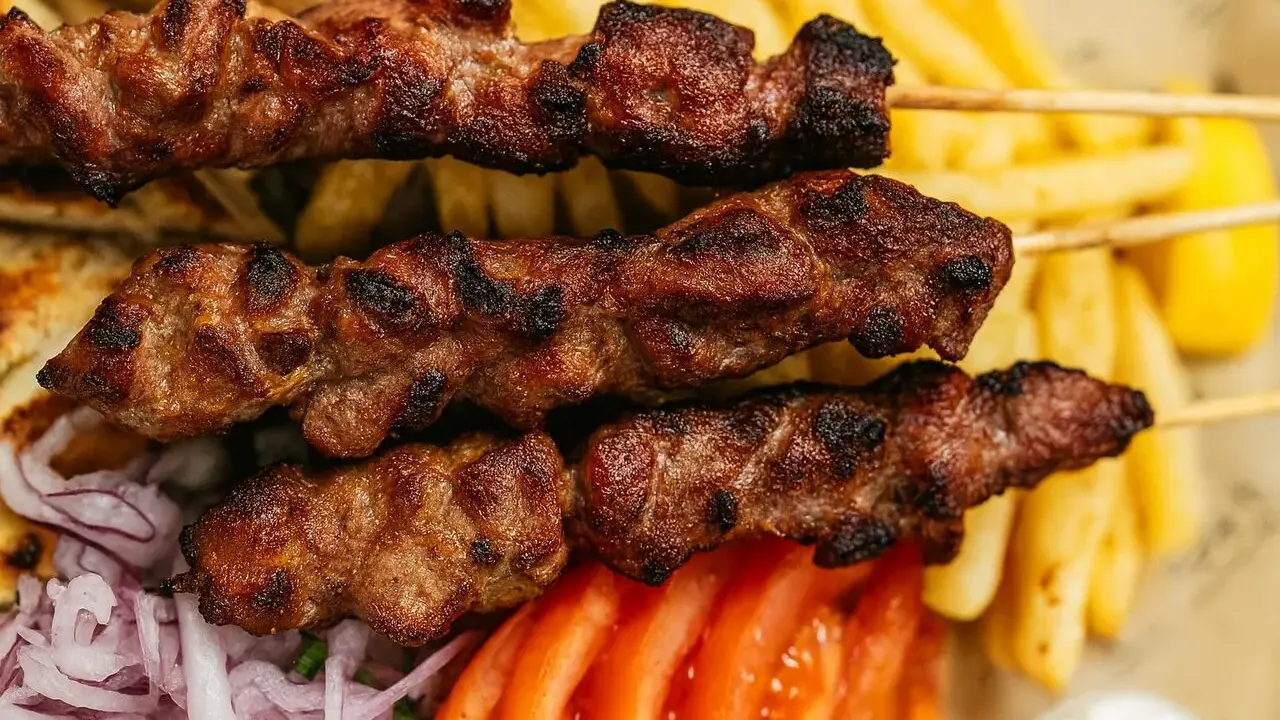 Brochettes de viande grillée, parfaites pour une cuisson indirecte au barbecue, accompagnées de frites, pain pita, tomates et oignons.