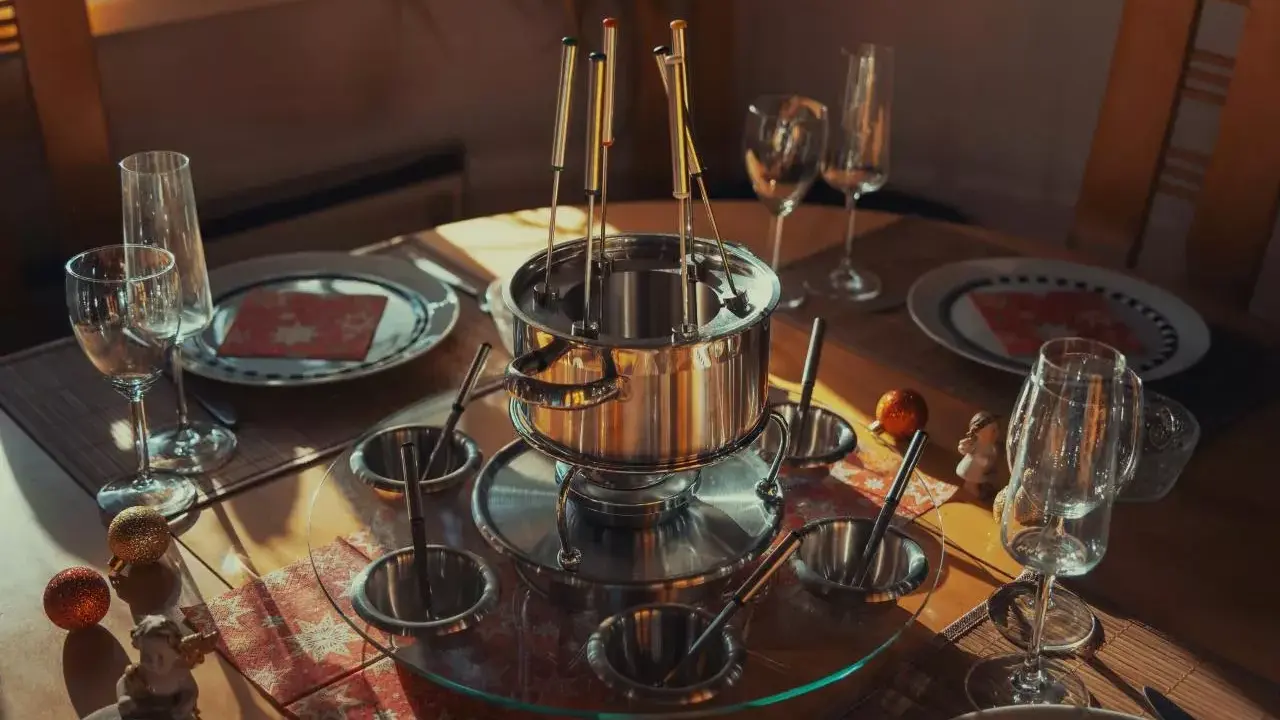 Service à fondue prêt pour un repas convivial. Le caquelon en inox est entouré de coupelles et de fourchettes, promettant une fondue sans huile savoureuse.