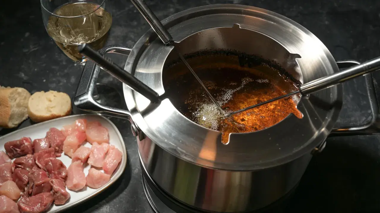 Préparation pour comment faire une fondue bourguignonne : morceaux de viande crue, pain et huile chaude dans le caquelon.