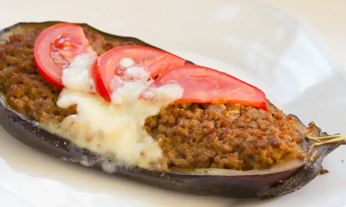 Aubergine farcie à la viande hachée, gratinée au fromage et garnie de rondelles de tomate. Une recette savoureuse et réconfortante.