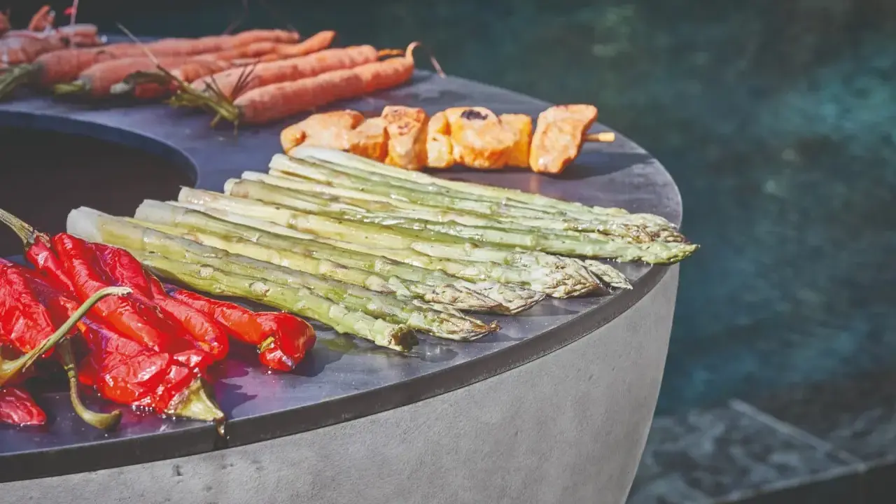 Légumes et brochettes de poulet sur un brasero, prêts pour une recette estivale. Carottes, poivrons rouges, asperges et poulet grillé.