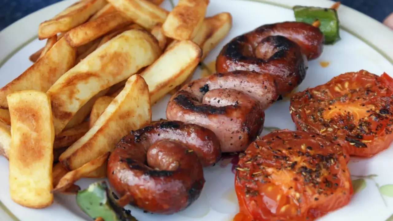 Assiette de saucisse à la plancha, frites dorées et tomates grillées. Un délice estival !