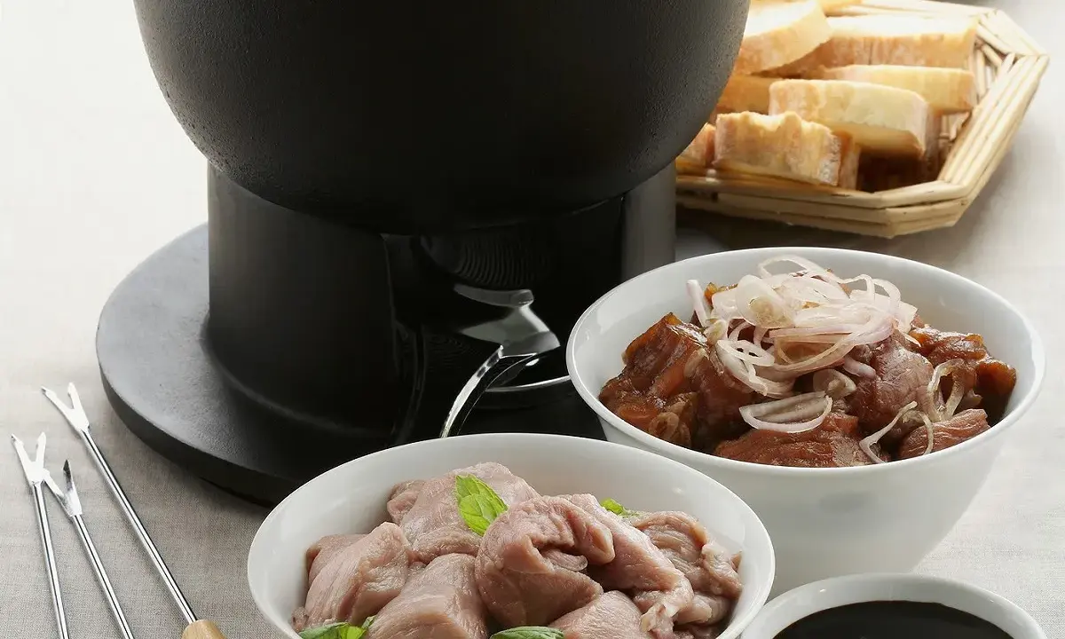 Préparation d'une fondue bourguignonne : viande blanche crue, viande cuite, pain et sauce. Des fourchettes à fondue sont prêtes.