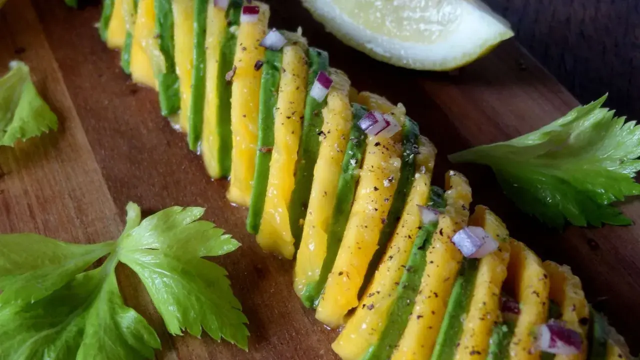 Une belle recette avocat et mangue, assaisonnée d'oignon rouge et de poivre, sur une planche en bois.