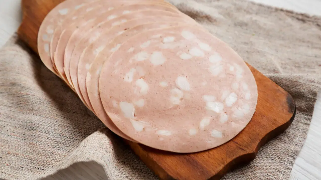 Tranches de mortadelle cuit ou cru, disposées en éventail sur une planche à découper en bois, sur un tissu de lin.
