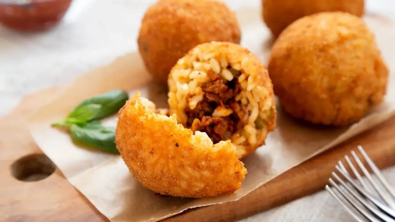 Arancini dorés et croustillants, un délice de la recette arancini, servis avec du basilic frais.