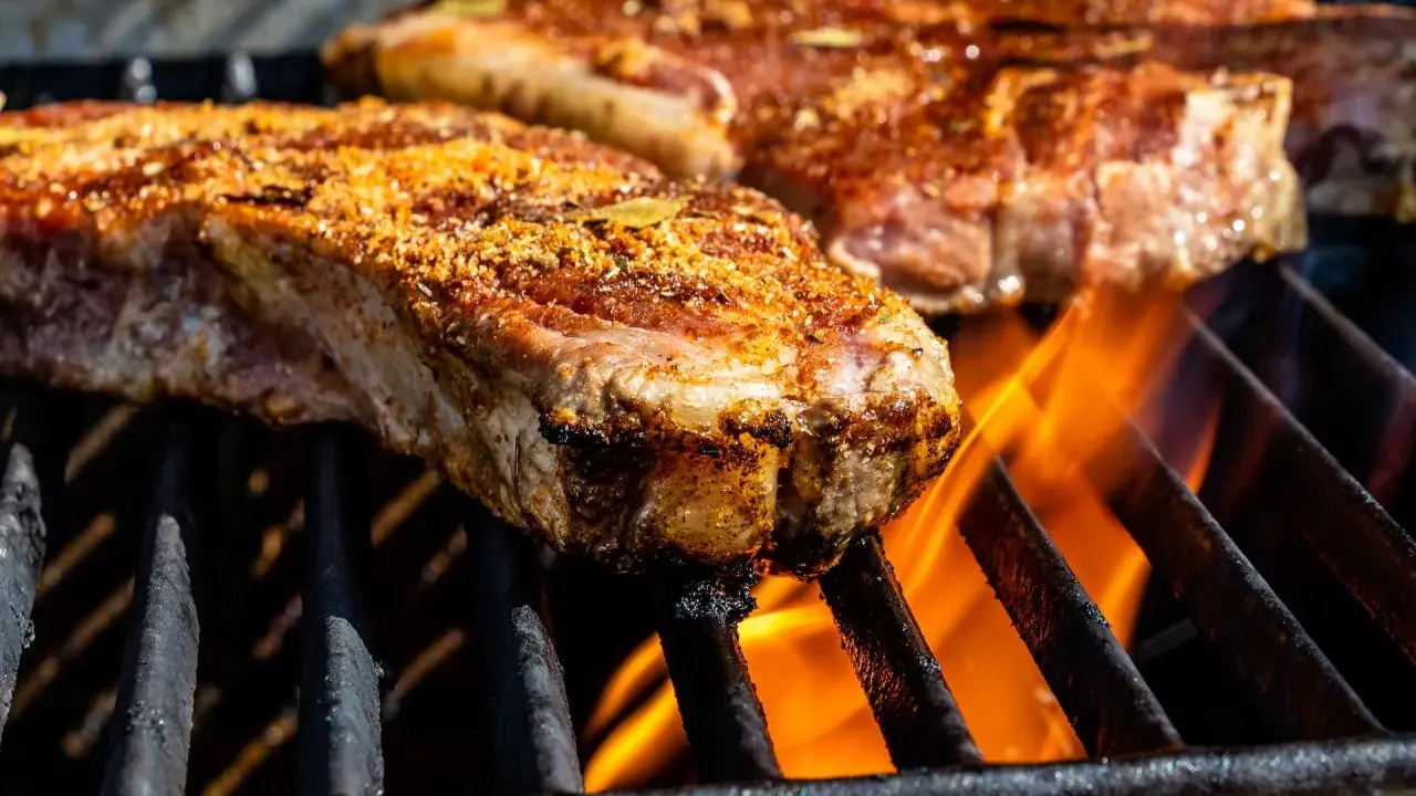 Deux entrecôtes savoureuses en cuisson sur un barbecue, les flammes dansent sous la viande.
