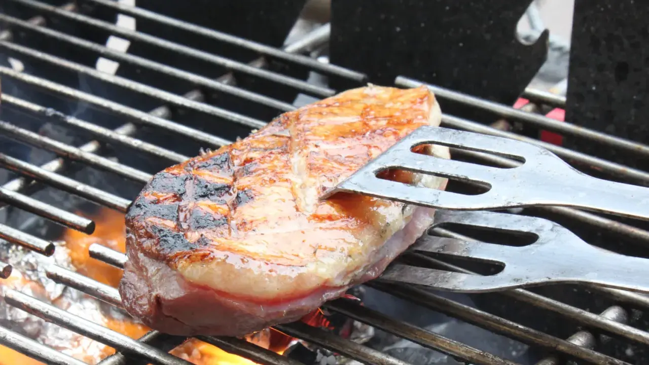 Magret de canard en cuisson indirecte sur un Weber, retourné avec une spatule. La peau est grillée et dorée, la chair rosée.