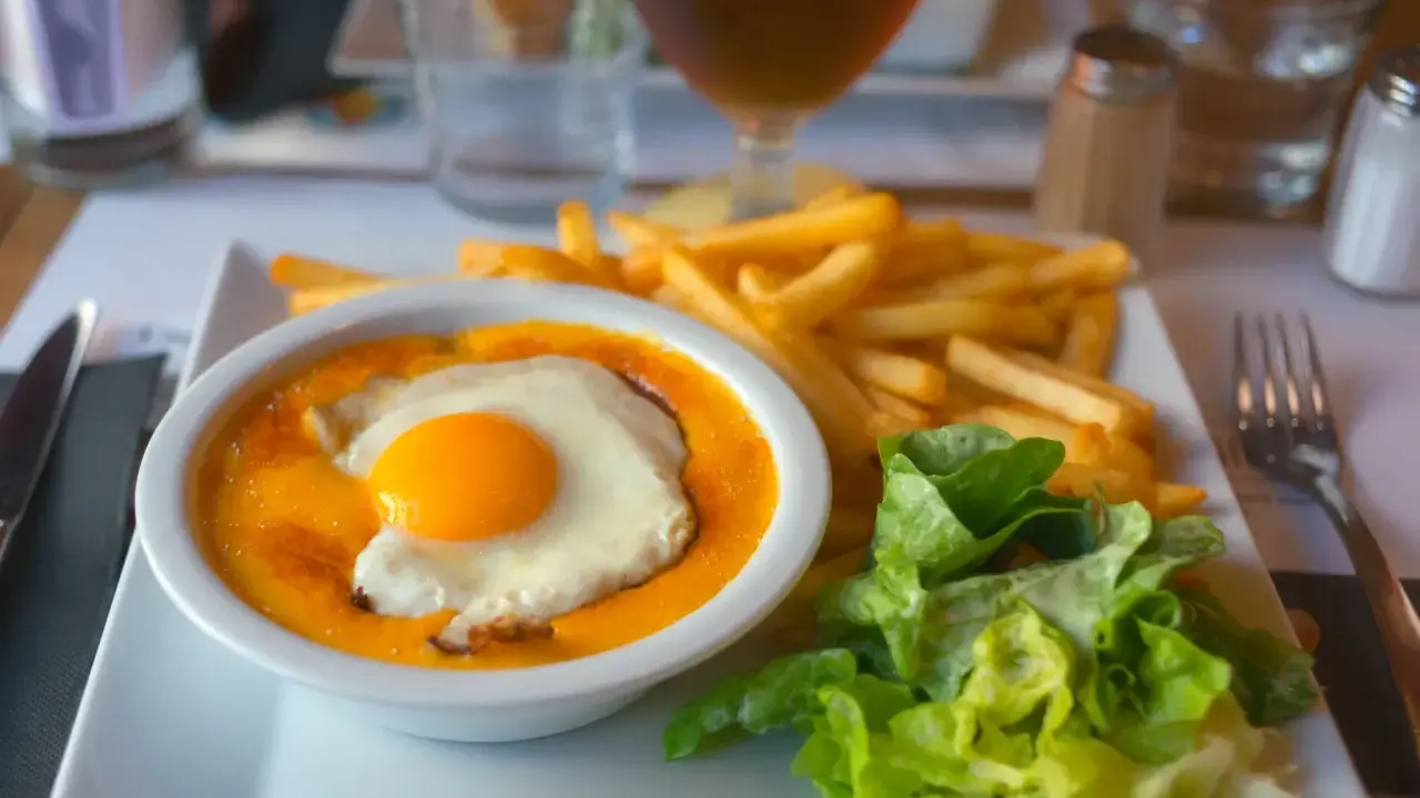 Un plat savoureux avec un œuf au plat sur une sauce orangée, des frites dorées et une salade verte. Un vrai délice, on se demande d'où vient le welsh !