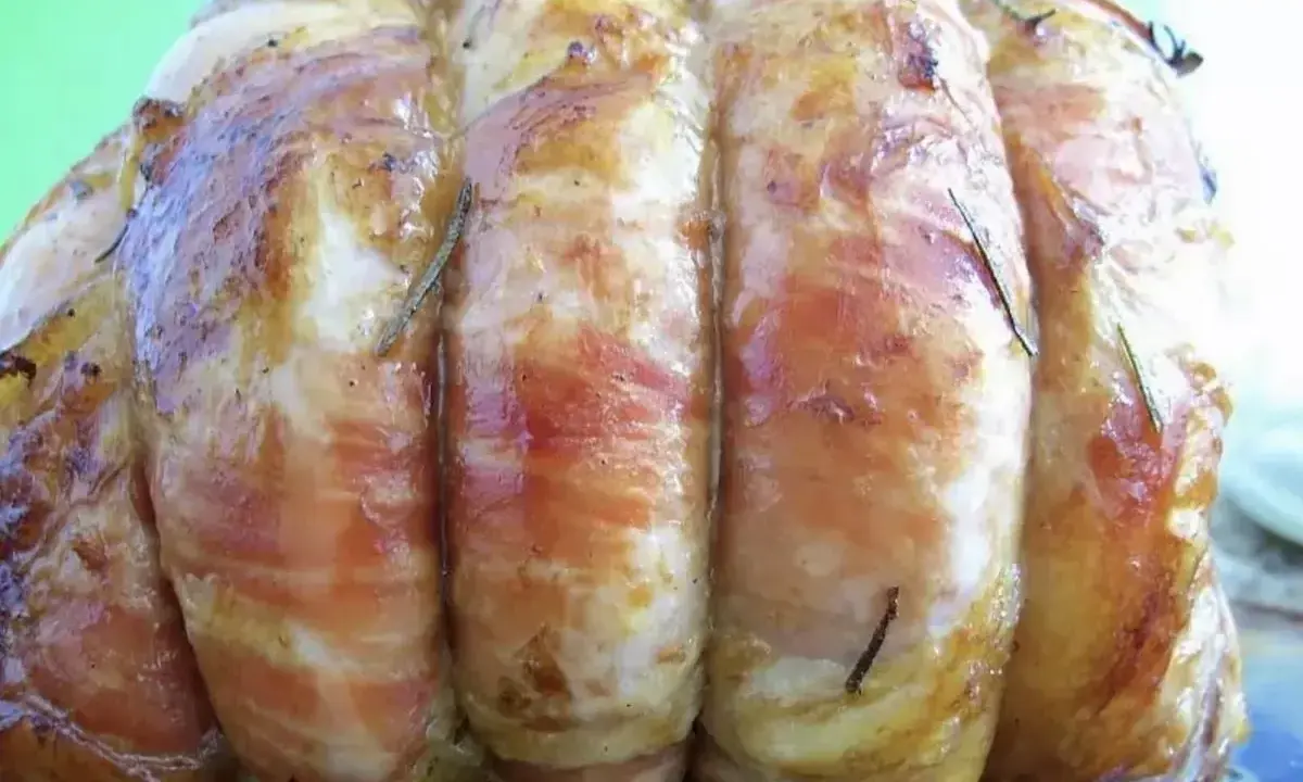 Un rôti de veau savoureux, enveloppé de lard et parsemé de romarin, prêt à être dégusté.