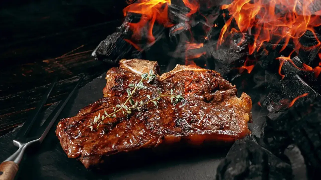 Un steak T-bone juteux, garni de thym, cuit sur des braises ardentes. Une parfaite recette barbecue pour les amateurs de viande.