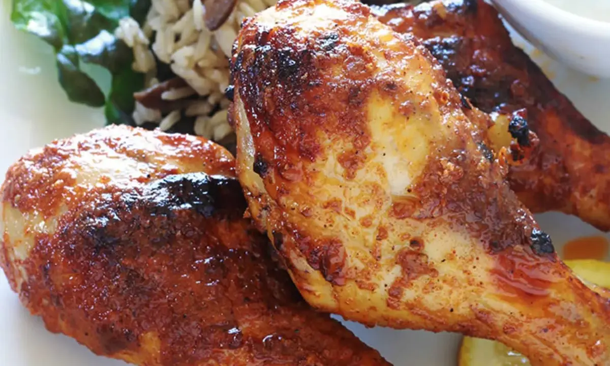 Trois pilons de poulet grillés et dorés, servis avec du riz et une tranche de citron.