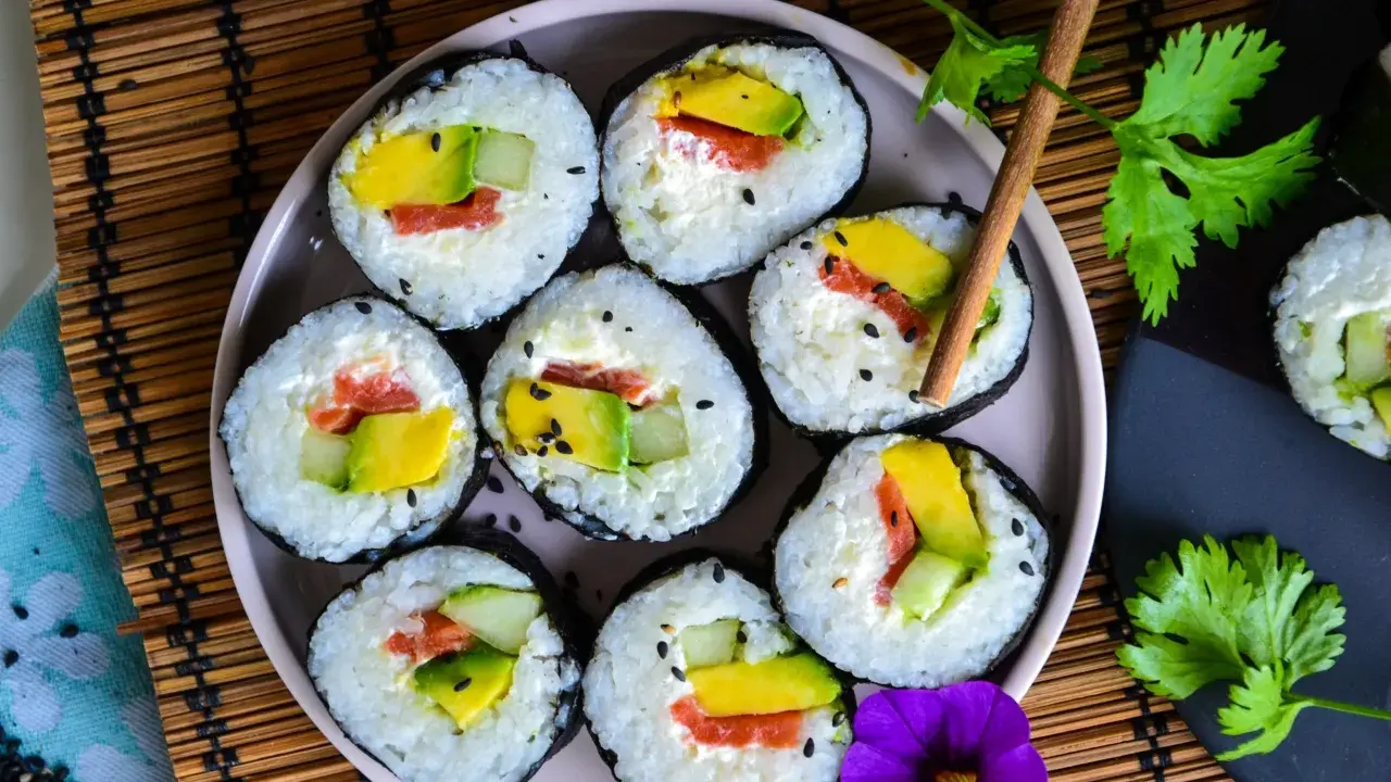 Assiette de makis frais, parfaits pour une recette sushi maison. Avocat, saumon et concombre roulés dans du riz et des algues, parsemés de graines de sésame.