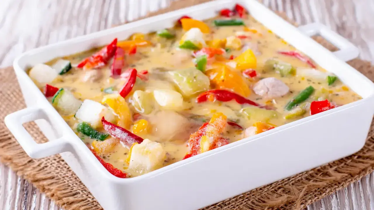Un gratin de légumes coloré et crémeux, avec des poivrons, courgettes et autres légumes dans une sauce onctueuse, prêt à être dégusté.