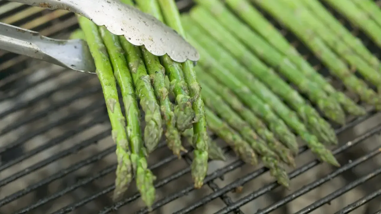 Des asperges vertes grillées, parfaites pour une recette simple et savoureuse. Les pinces saisissent un bouquet prêt à être retourné.