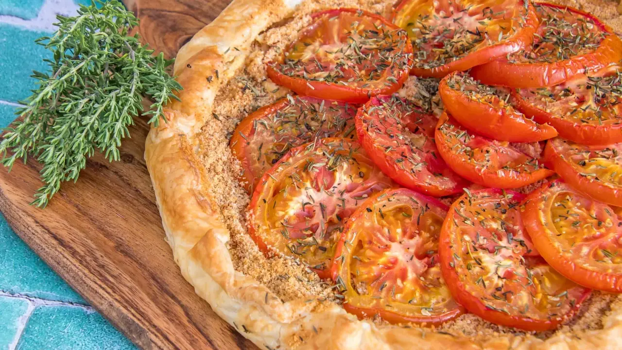 Une délicieuse tarte tomates aux herbes, sur une planche en bois, avec une branche de thym frais à côté.