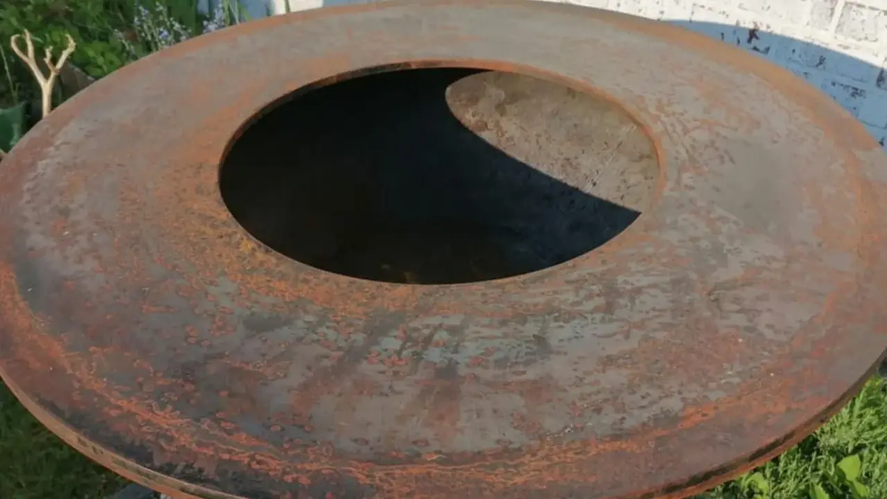 Gros plan sur le plateau rouillé d'un brasero, prêt pour son culottage. La surface métallique présente des nuances orangées et grises.