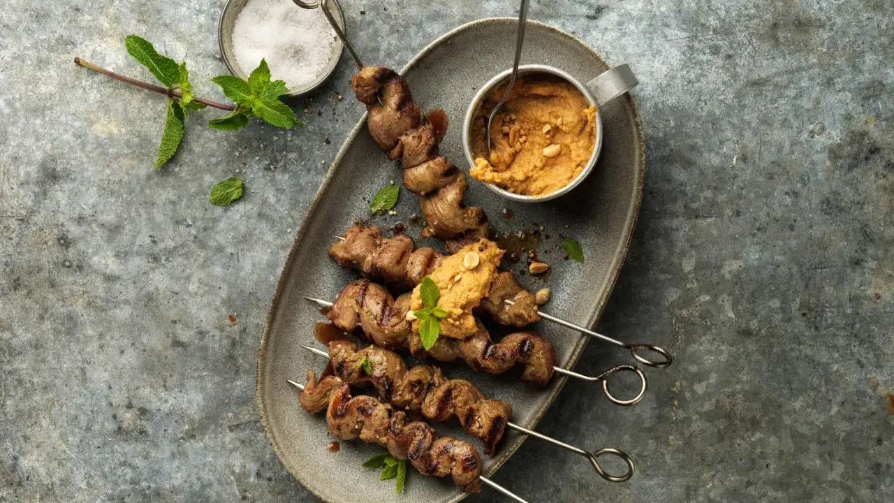 Brochettes d'agneau grillées au barbecue, servies avec une sauce aux arachides et garnies de menthe fraîche.