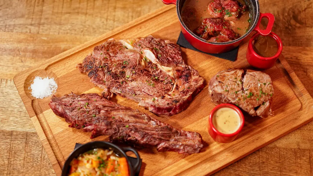 Assortiment de viande à griller, steak, et ragoût de bœuf, servi avec des sauces et des légumes sur une planche en bois.