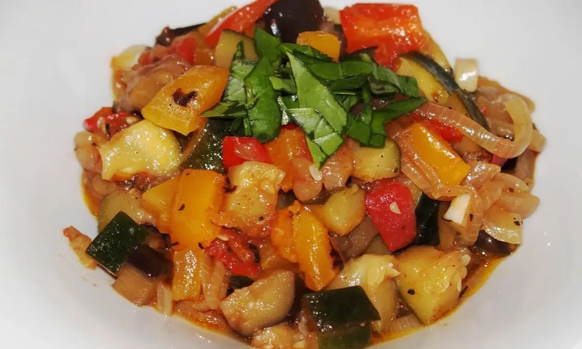 Un plat coloré de ratatouille recette, avec des dés de courgettes, aubergines, poivrons et tomates, garni de basilic frais.