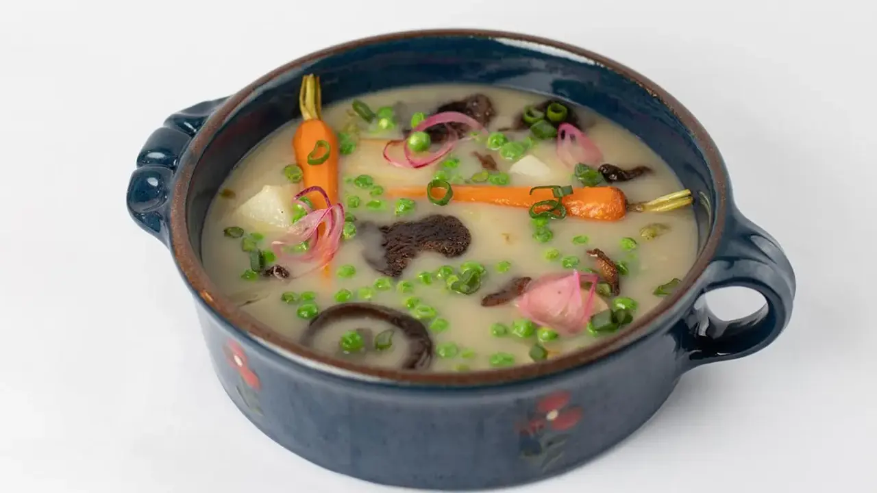 Délicieuse recette végétarienne : un potage crémeux aux carottes, petits pois, pommes de terre et champignons, garni d'oignons rouges et de ciboule.