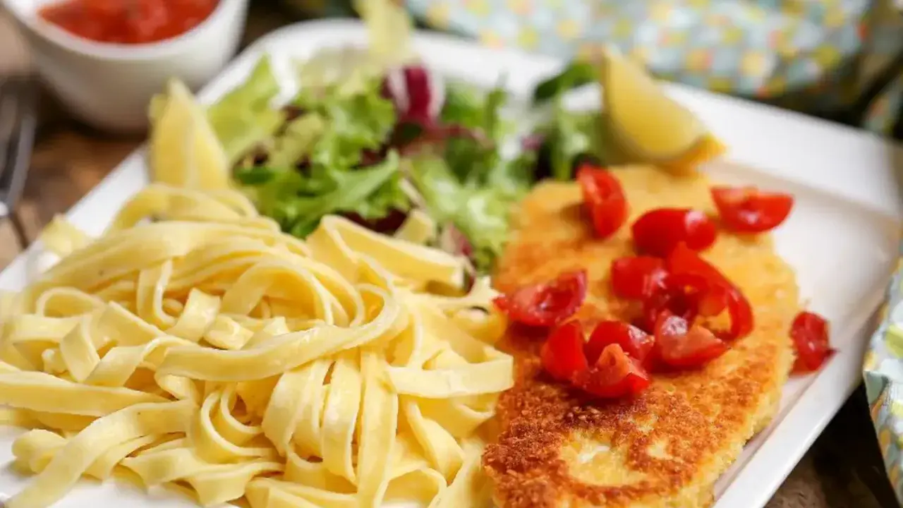 Une assiette de pâtes fraîches, une escalope milanaise dorée garnie de tomates cerises, et une salade verte. Un délice !