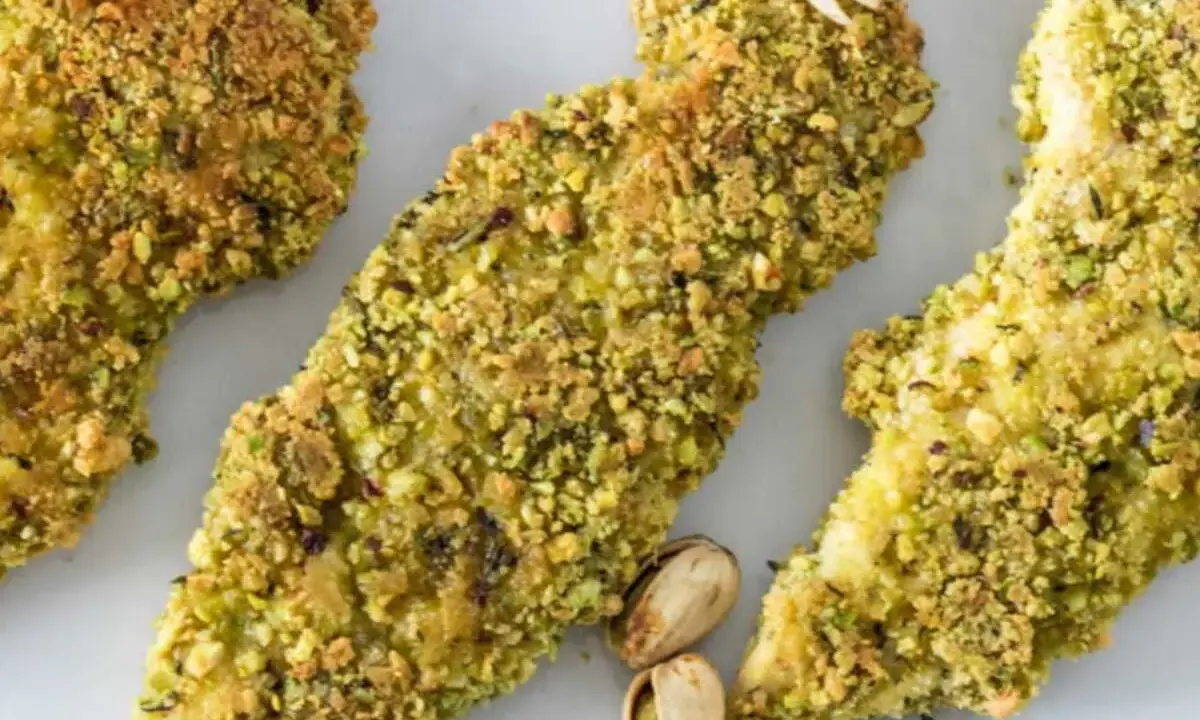 Trois tendres morceaux de poulet pistache, croustillants et dorés, sont présentés sur fond blanc.