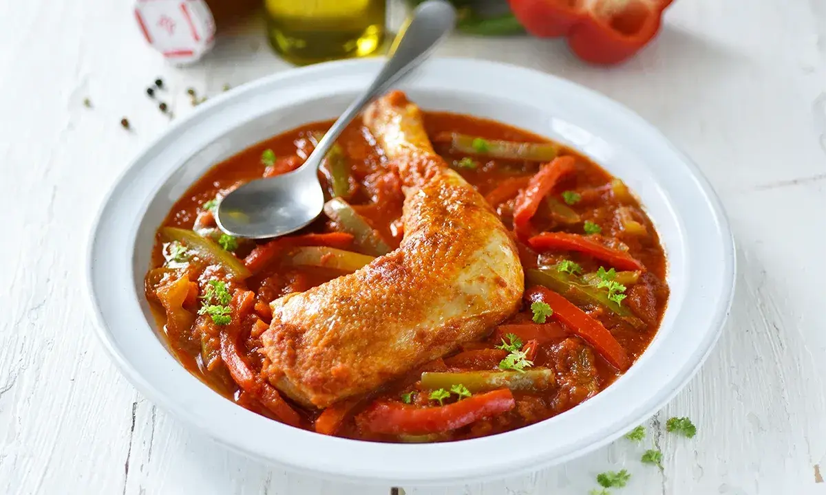 Un plat de poulet basquaise savoureux, avec un morceau de poulet doré dans une sauce tomate riche aux poivrons rouges et verts, garni de persil frais.