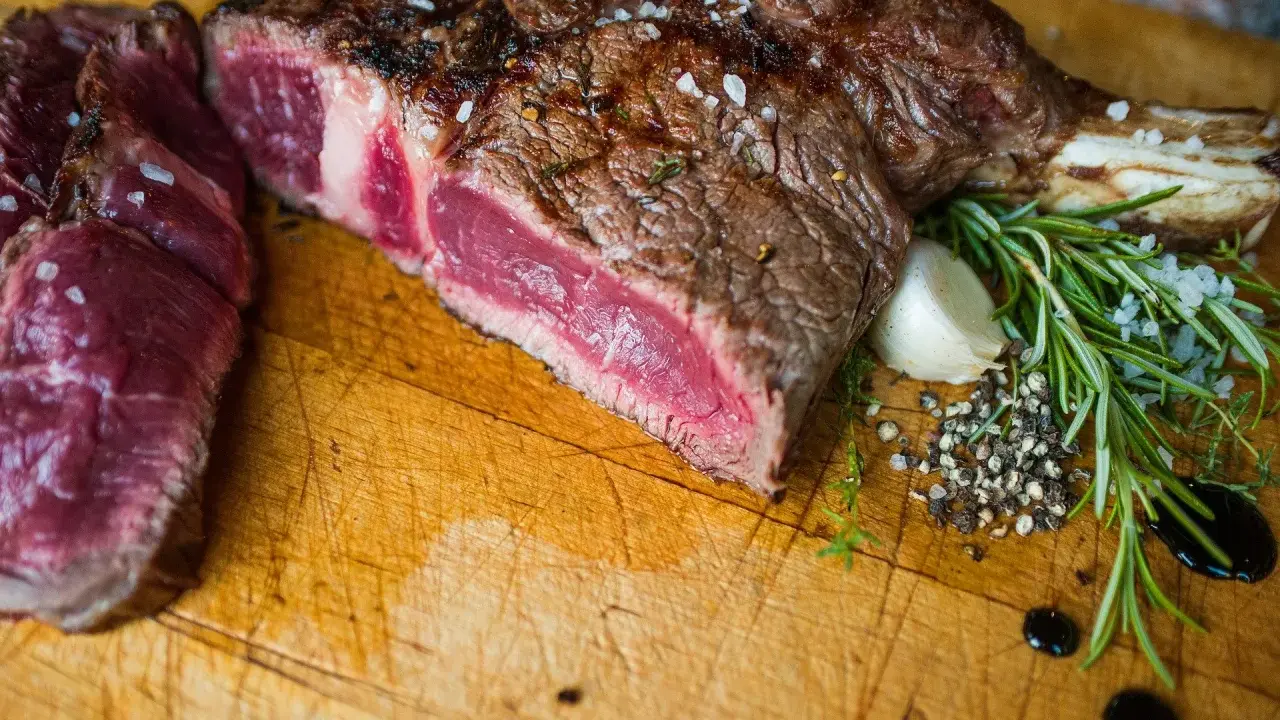Un succulent côte de bœuf barbecue, saignant et parsemé de gros sel, est prêt à être dégusté. Accompagné de romarin frais, d'ail et de poivre concassé.
