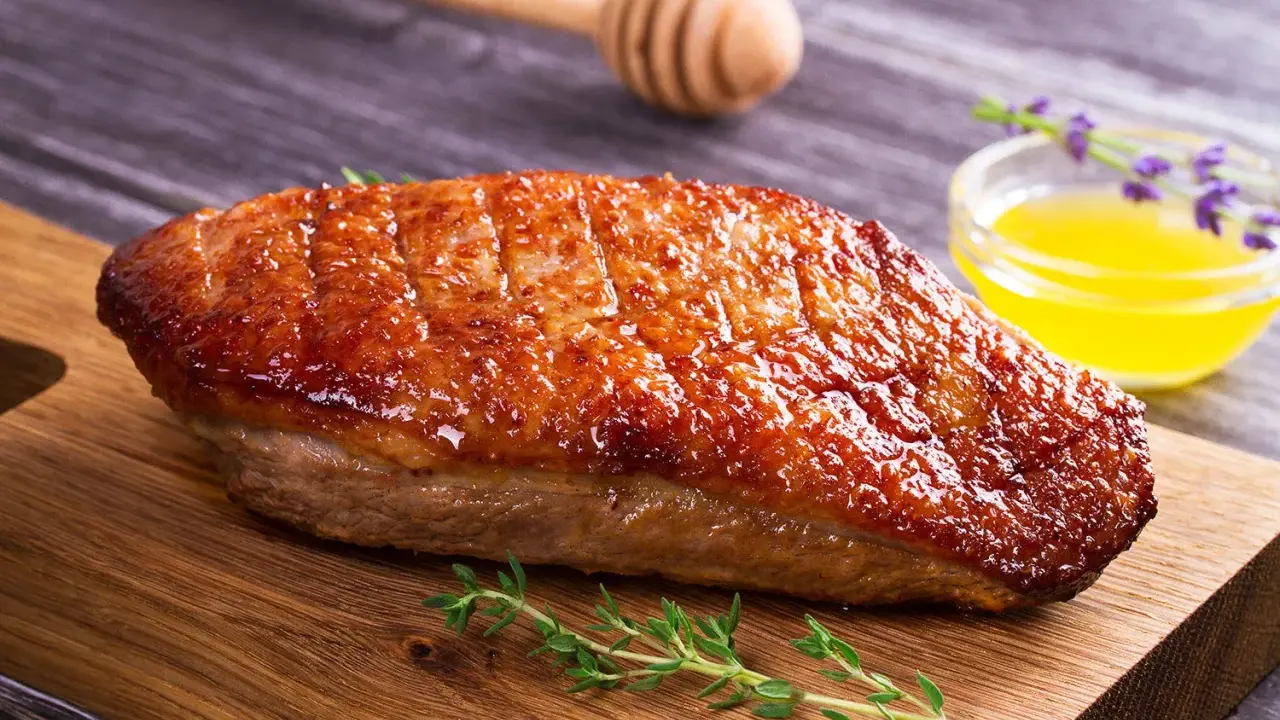 Un magret de canard au barbecue, la peau dorée et croustillante, servi sur une planche en bois avec du thym frais et une sauce au miel.