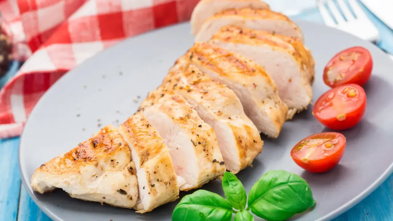 Un délicieux filet de poulet grillé, tranché et servi avec des tomates cerises et du basilic frais sur une assiette grise.
